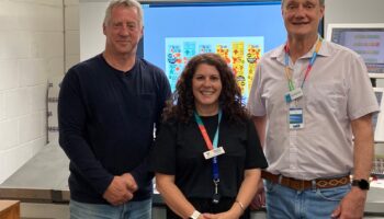 An image of three people standing in front of a printing machine